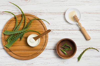 Aloe vera skincare flat lay with fresh aloe leaves, a bowl of natural aloe gel, and honey on a rustic white wooden table — highlighting natural remedies for hydration and healing.