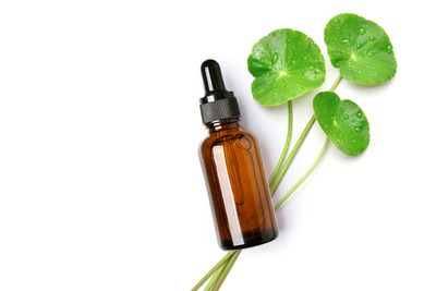 Brown dropper bottle with fresh Centella Asiatica (cica) leaves on a white background, representing natural skincare.