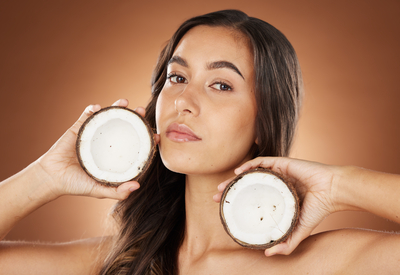 Woman holding coconut halves near her face — illustrating coconut oil in skincare, hydrating benefits vs pore-clogging risk.