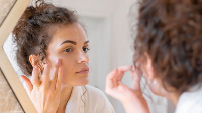 Woman applying moisturizer in a mirror—illustrating dry vs. dehydrated skin, hydration, and skin barrier repair skincare routine.