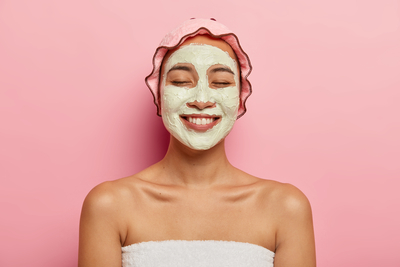 Smiling woman wearing a green clay face mask and towel headband — testing an acne-safe, non-comedogenic clay mask for pore cleansing.