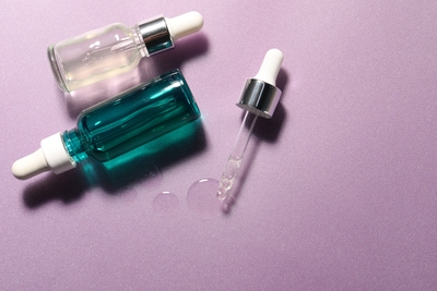 PHA skincare serums in glass dropper bottles on a pastel background, illustrating gentle exfoliating acids like gluconolactone and lactobionic acid for sensitive skin.