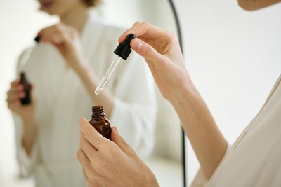Close-up of a woman using a dropper to apply niacinamide serum as part of her daily skincare routine in front of a mirror