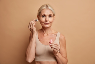 Mature woman applying serum to her face as part of her skincare routine.