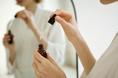 Woman using a dropper to apply niacinamide serum in front of a mirror as part of her skincare routine