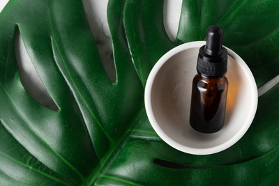 Amber dropper bottle with squalane oil in a white bowl on top of a large green leaf, representing natural skincare