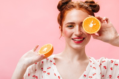 Smiling woman holding orange halves, symbolizing Vitamin C and its brightening benefits for skincare