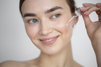 Smiling woman applying salicylic acid serum to her cheek with a dropper as part of a skincare routine