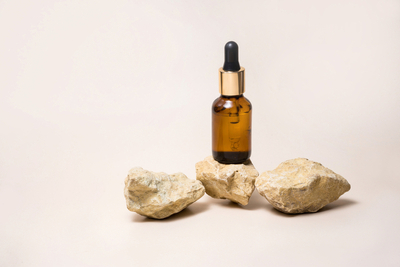 Retinol serum bottle with gold dropper displayed among beige stones on a light neutral background, representing skincare essentials.