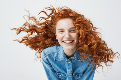 Smiling woman with fair skin and red hair, representing rosacea-prone skin.